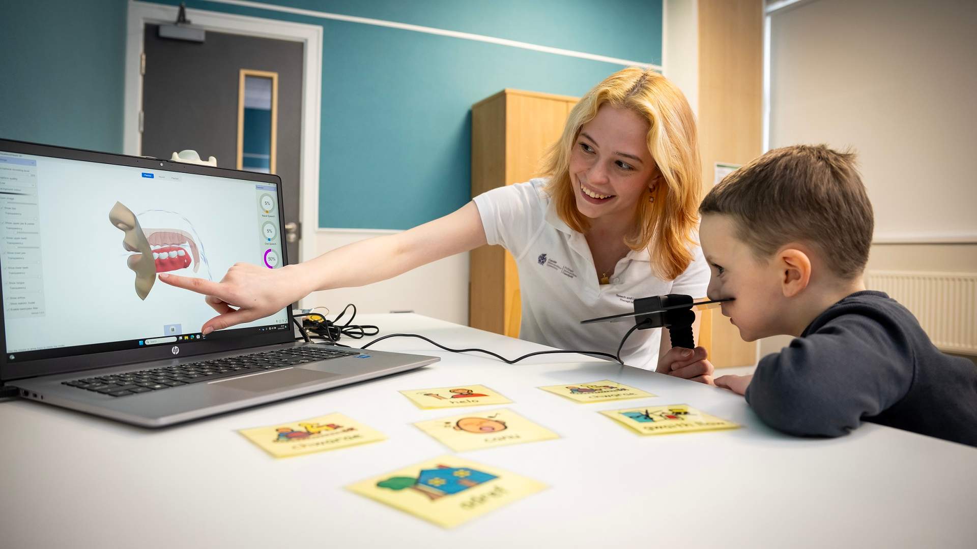 A young woman points to a laptop screen in an educational moment for the young child sat next to them