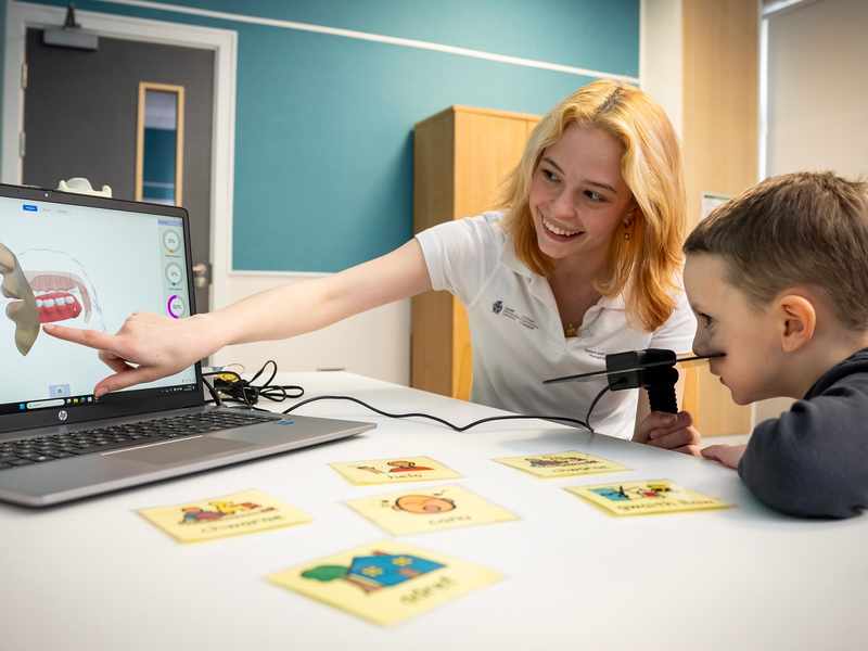 A young woman points to a laptop screen in an educational moment for the young child sat next to them