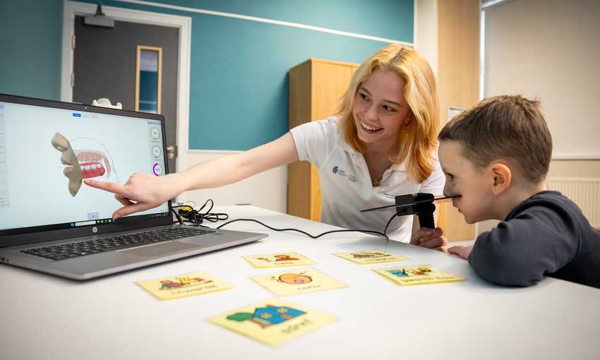 A young woman points to a laptop screen in an educational moment for the young child sat next to them