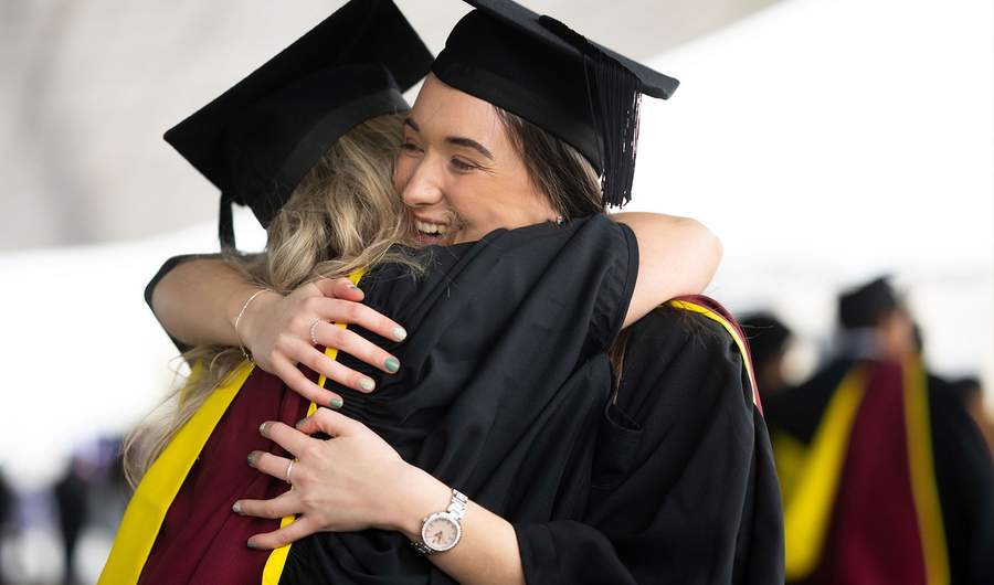 Two female graduates embrace joyfully, celebrating their achievements on graduation day.