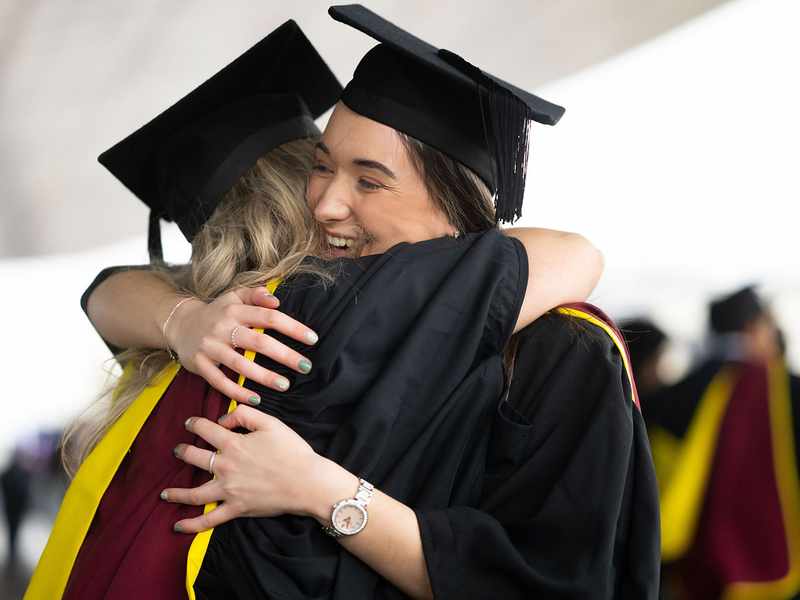 Two female graduates embrace joyfully, celebrating their achievements on graduation day.