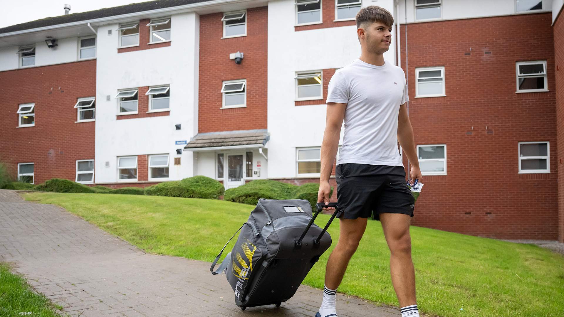 A student pulling a suitcase along a path, heading towards his student accommodation.