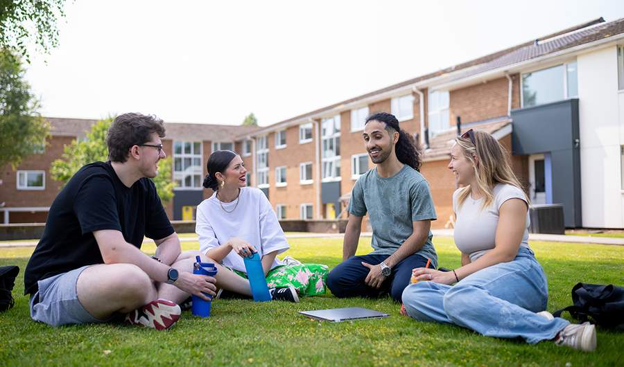 Group of four students sitting on the grass, chatting and laughing outside a student accommodation building