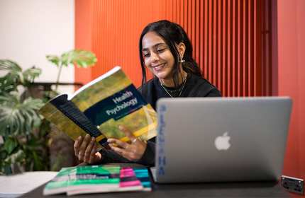 Aleysha Caffoor reading a book on Health Psychology, sat at a table