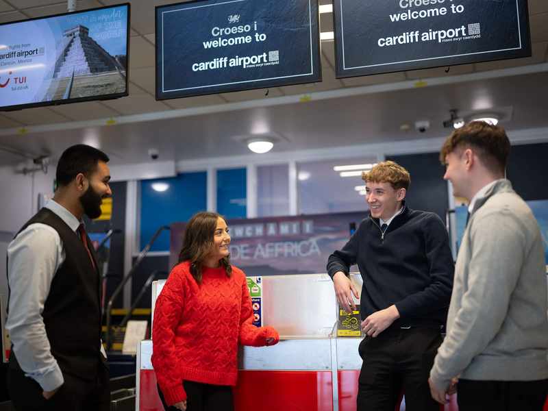 A group of people stand together talking next to an airport check-in desk.