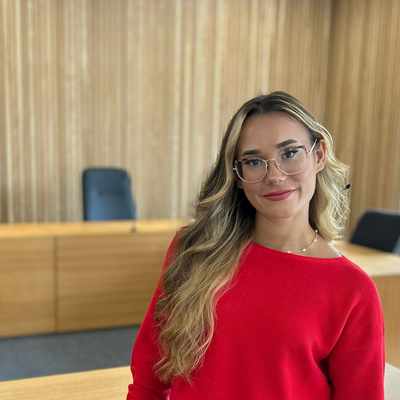 A group of six students is standing outside Cardiff Metropolitan University. One student is taking a selfie while the others smile and pose. The university building is visible in the background under a partly cloudy sky.