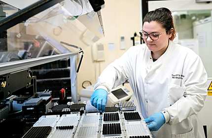 Student in white laboratory overalls works at a large scientific machine