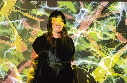 Audrey Shaw stands in front of a wall on which is projected a green, yellow and pink pattern