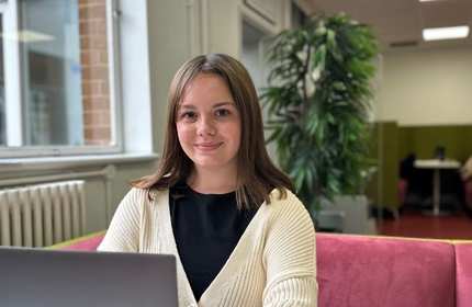 A person sits on a sofa. In front of them is an open laptop computer.