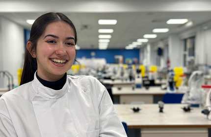 Claudia Luthra, wearing white a laboratory jacket, stands in a biomedical laboratory