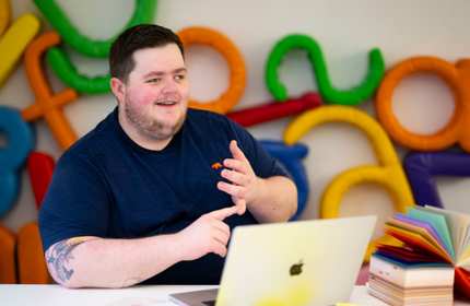 A person sits at a table. In front of them is an open laptop computer.