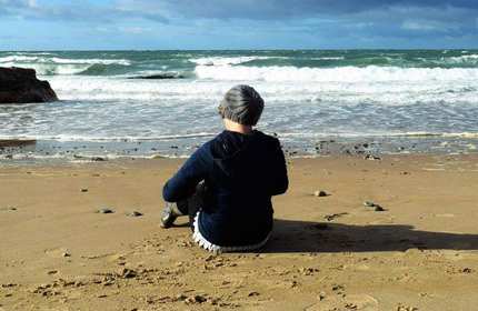 A person sits on a beach, looking out at the sea.