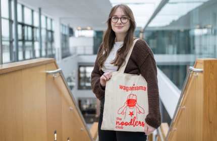 Jenny Virgo stands at the top of a set of stairs showing a branded tote bag