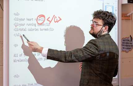 Joseph Hamer gestures with a pen to an interactive whiteboard while giving a lesson in a school classroom
