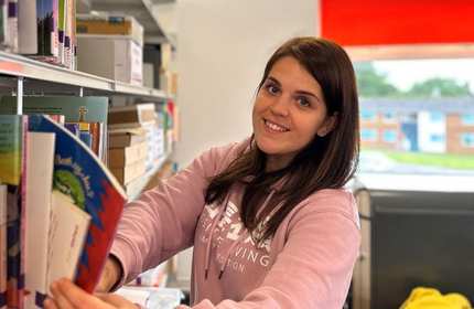 Katie places a book on the bookshelf