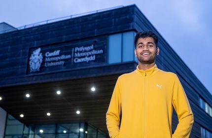 Kush Shinde stands with arms in their jacket pockets outside the Cardiff School of Management