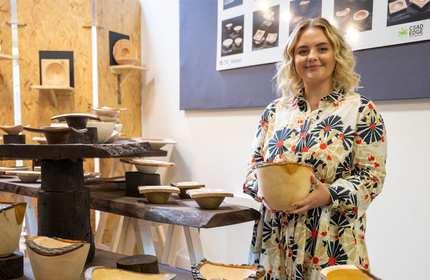 A person holds a carved bowl. A number of similar bowls on wooden stands surround them.
