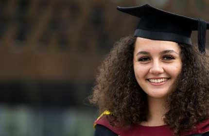 A person wearing a graduation cap and gown. Behind them is the Wales Millennium Centre.