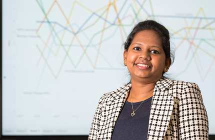Merlin wearing a top and suit jacket, stands in front of a presentation board displaying a complex graph