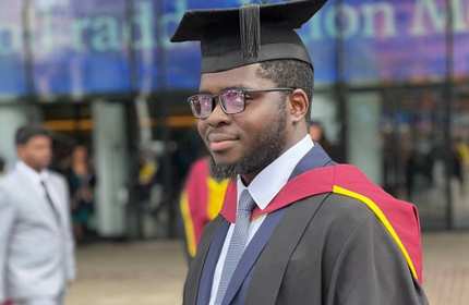 Olugbenga Adesanya stands wearing their graduate cap and gown during Gradiation day
