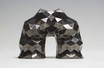 A silver geometric sculpture, resembling an arch and crafted from a metallic material