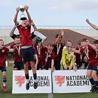 A group of young men joyfully holding up a trophy, celebrating winning a competition and enthusiasm for the sport.