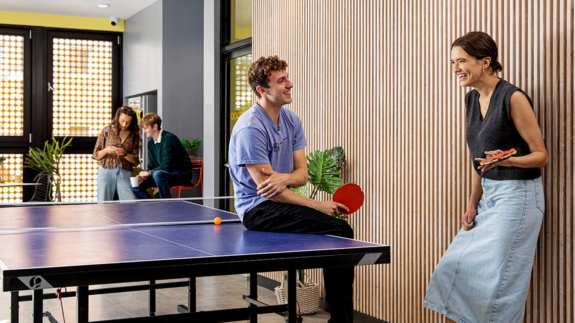 Two individuals playing ping pong in a communal area, showcasing a fun break from studying in a collaborative environment.