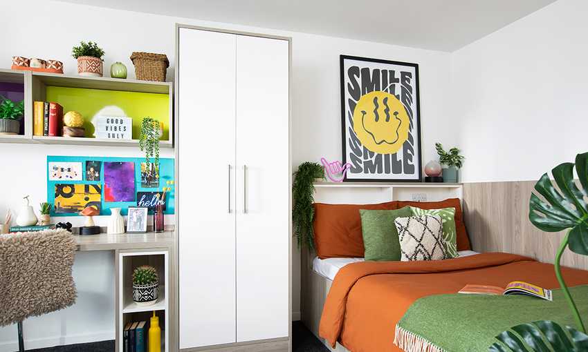 A cozy bedroom featuring a bed, a desk, and a green plant in the corner, creating a serene atmosphere.