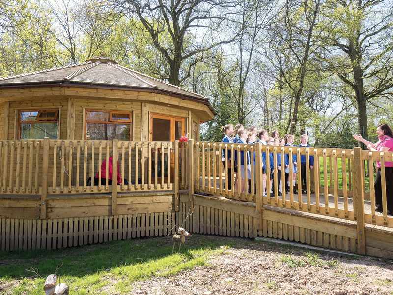 A group of children stand on a walkway leading to a small wooden building.
