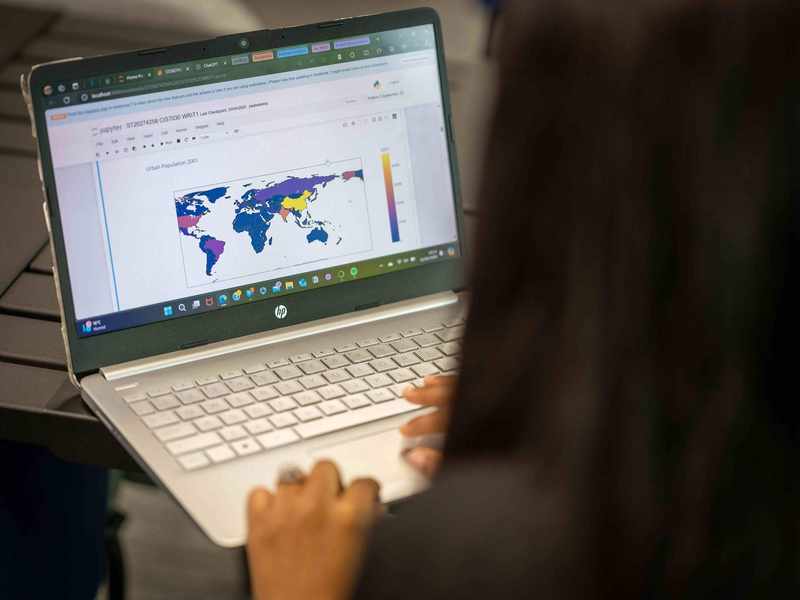 A close-up of a laptop computer. On the laptop screen is a map of the world.