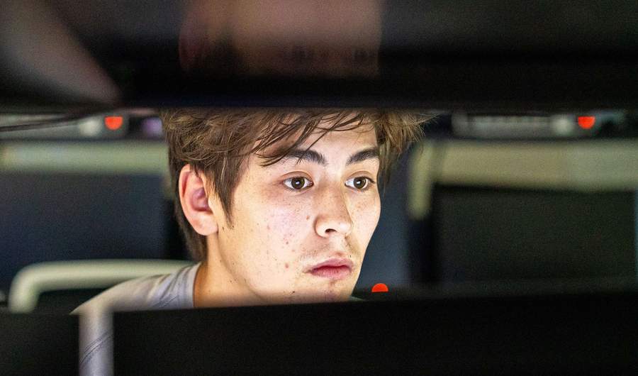 A close-up of a person looking at a computer monitor. Their face is lit from the light of the screen.