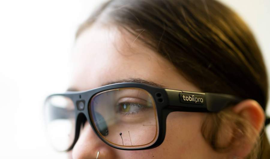 A close-up of a person wearing thick glasses. The glasses appear to have sensors on the front.
