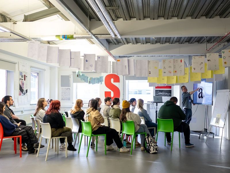 A group of young adults seated for a lecture in an open spaced workshop