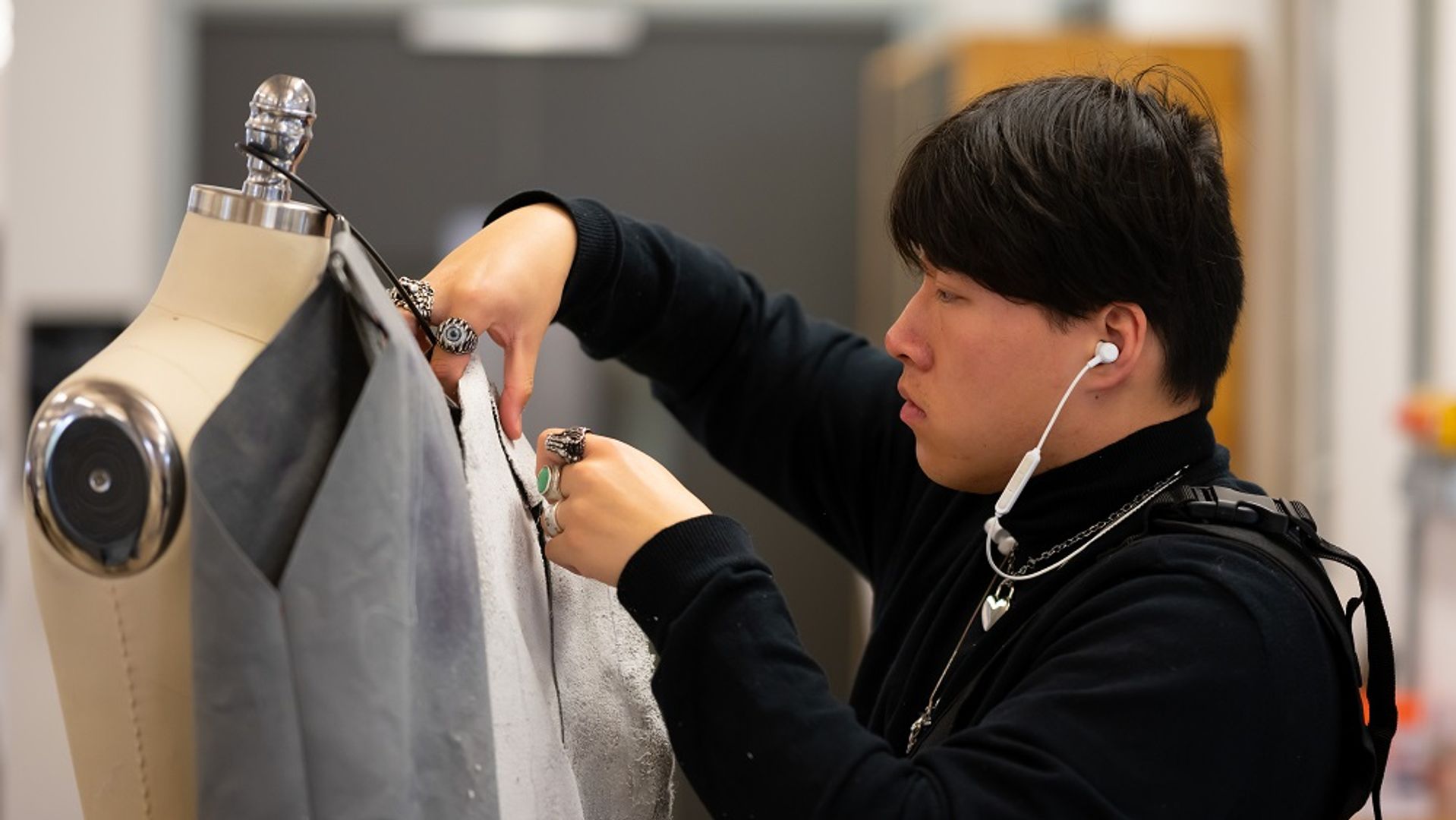 A young adult adjusts a piece of fabric dressed on a mannequin