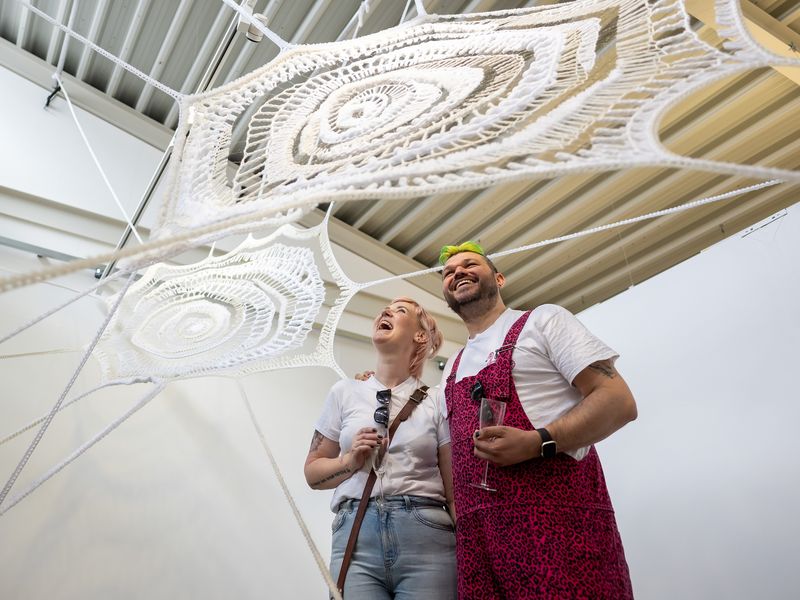 Two young adults stand underneath a large spiderweb art installation