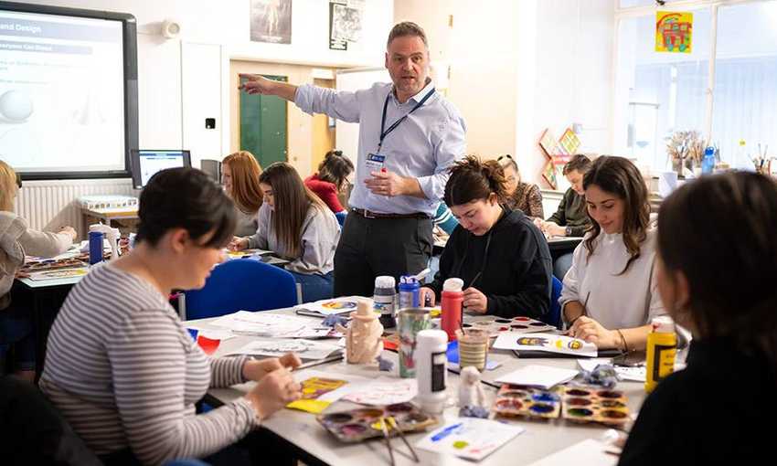 Teacher speaks to students painting around a table