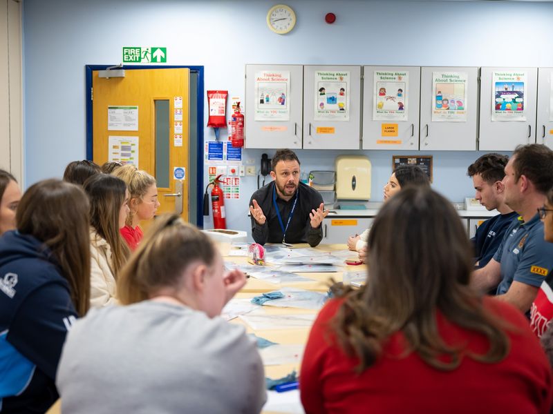 Teacher speaks to group of pupils around a classroom table