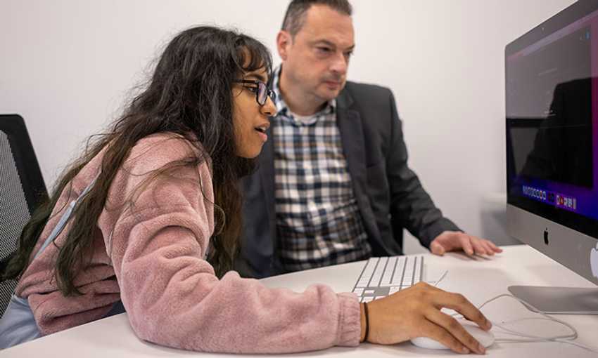 Student uses a keyboard and mouse to navigate on a computer screen as lecturer watches