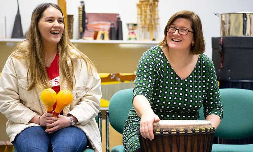 Student teacher and teacher sat smiling while holding musical instruments