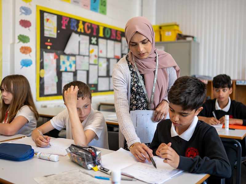 A teacher points to a pupils worksheet as they work in the classroom