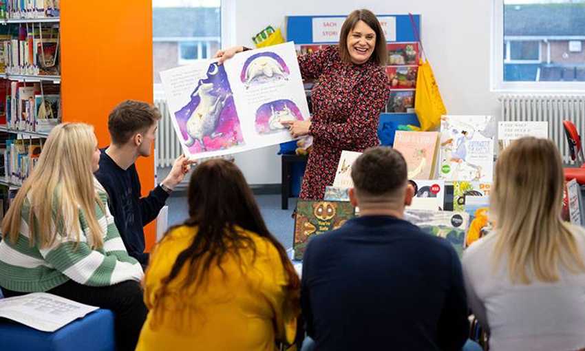 Teacher displays a story book in front of a classroom