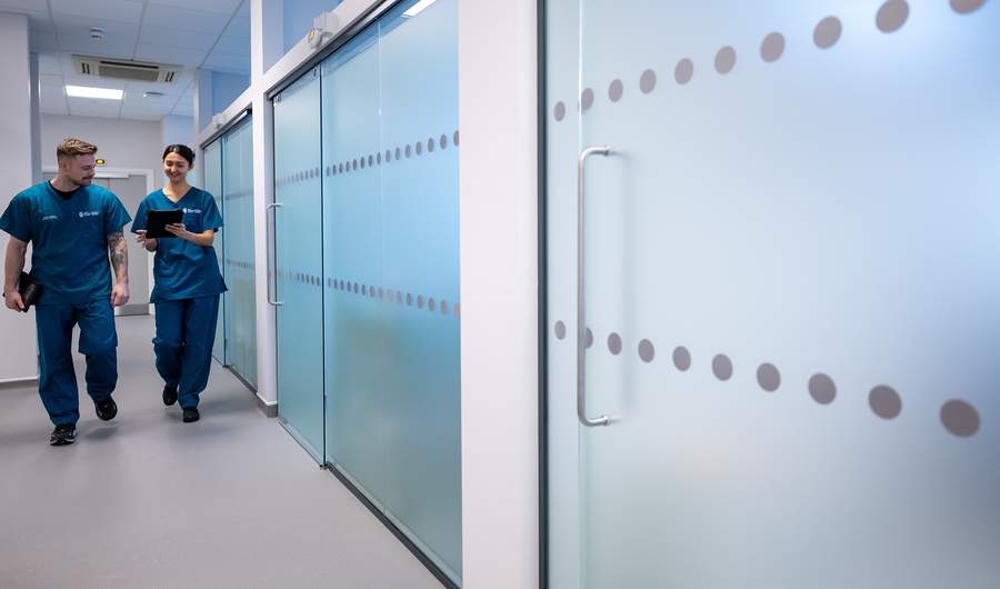 Two young adults in blue nursing scrubs walk through a corridor