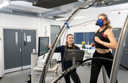 A young woman running on a treadmill is being monitored by another individual pointing at a screen during research