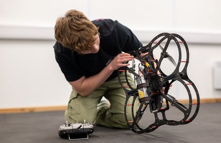 A young adult on their knees lift a drone to check on its wiring