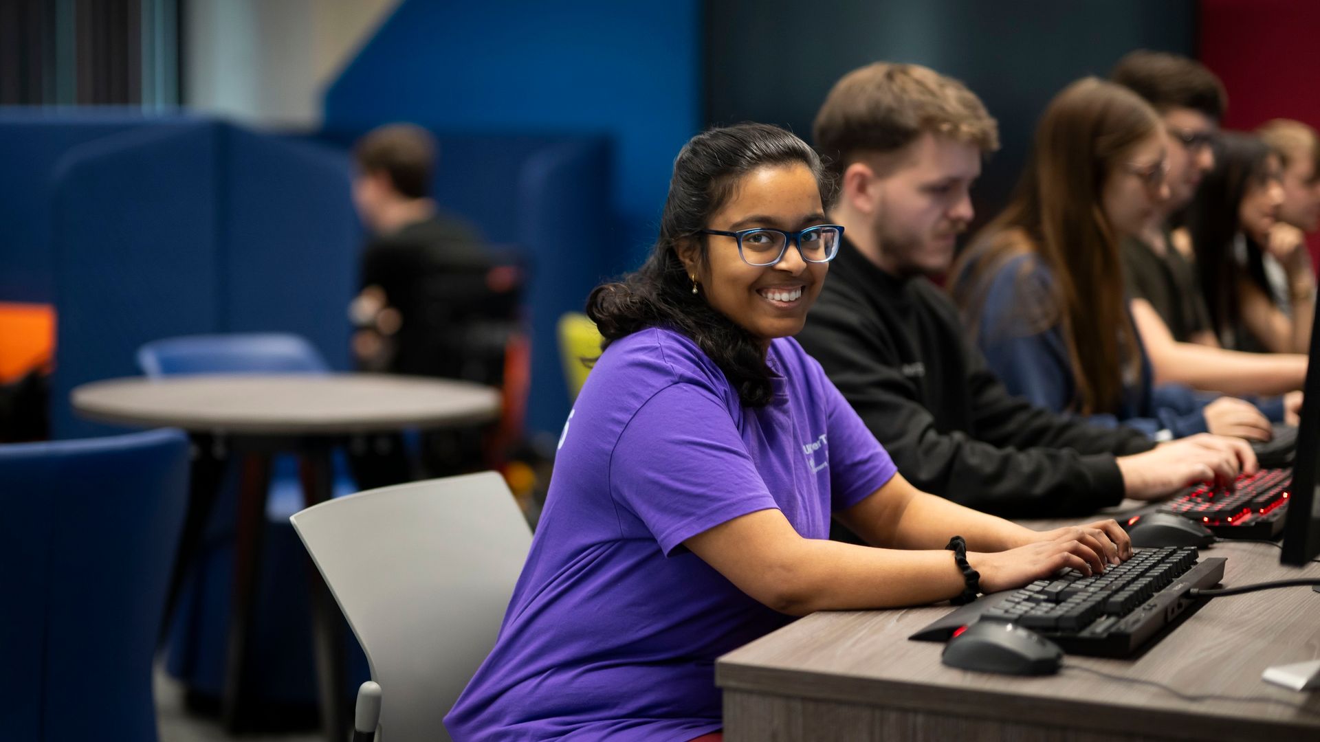 Row of students sat at their computer desks, with the closest smiling at the camera