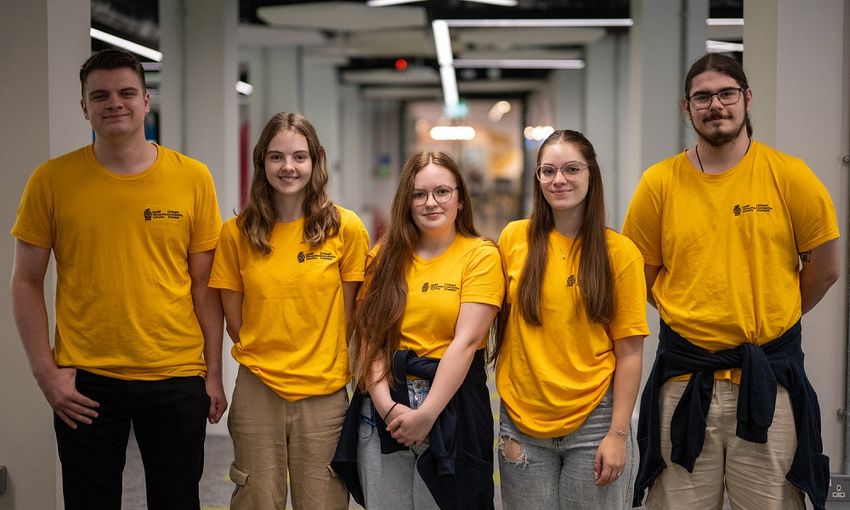 Five young adults in matching yellow t-shirts stand in a line