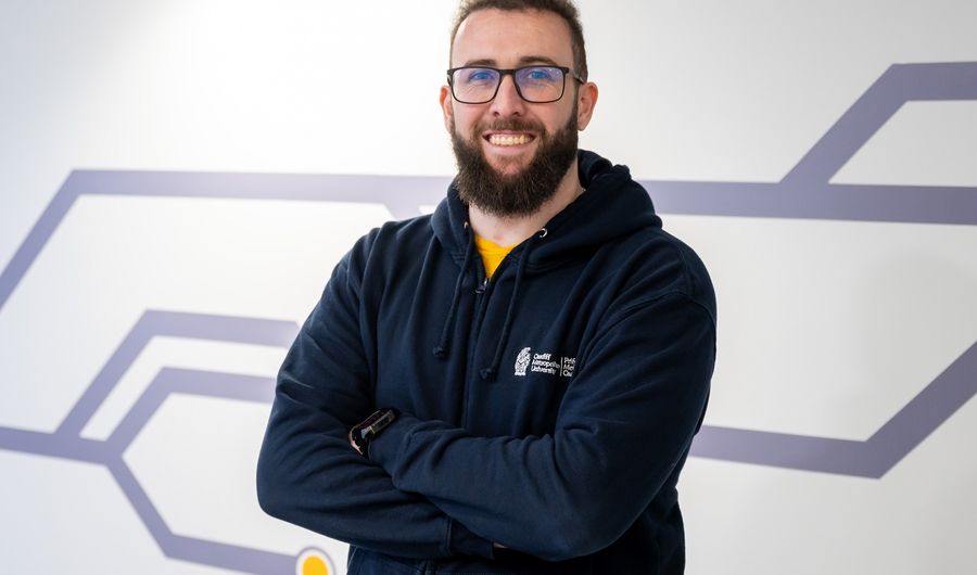 A student coach stands with his arms crossed smiling at the camera