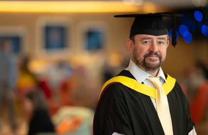 A man wearing a graduation gown and cap, celebrating his academic achievement with a proud smile.