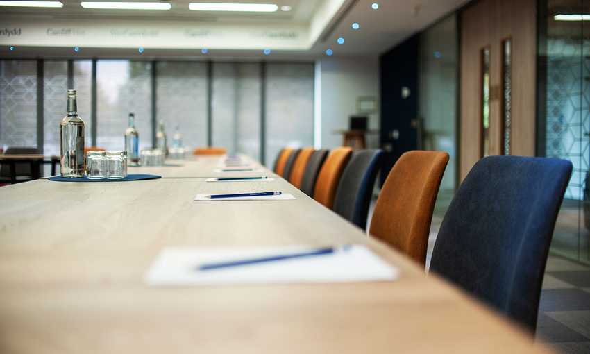 A conference table surrounded by chairs, featuring a bottle of water at the center, ready for a meeting.