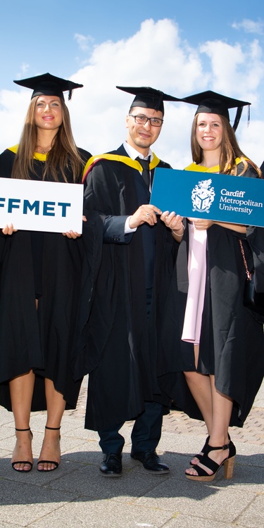 A group of students in graduation caps and gowns stand holding Cardiff Met signs